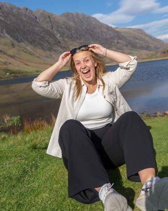 Young woman sitting on the ground at the waters of Glen Coe, Scotlnd