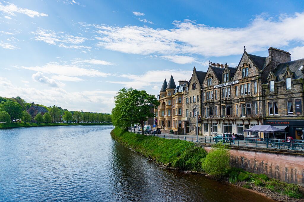 River Ness with lush green trees along its shores and stone buildings in Inverness
