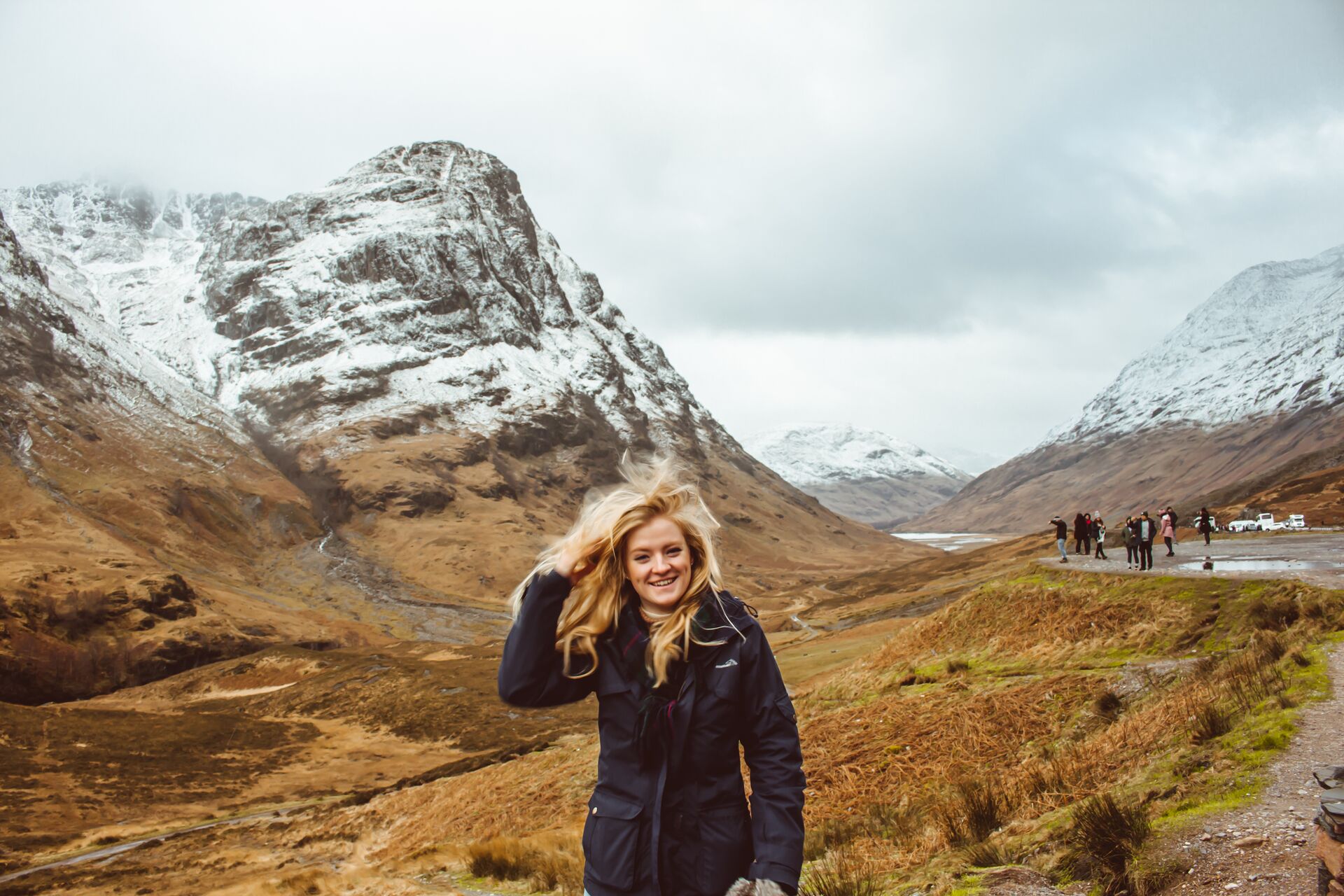 Young woman in winter at Glen Coe, hair blowing in the wind with snow-capped hills in the distance