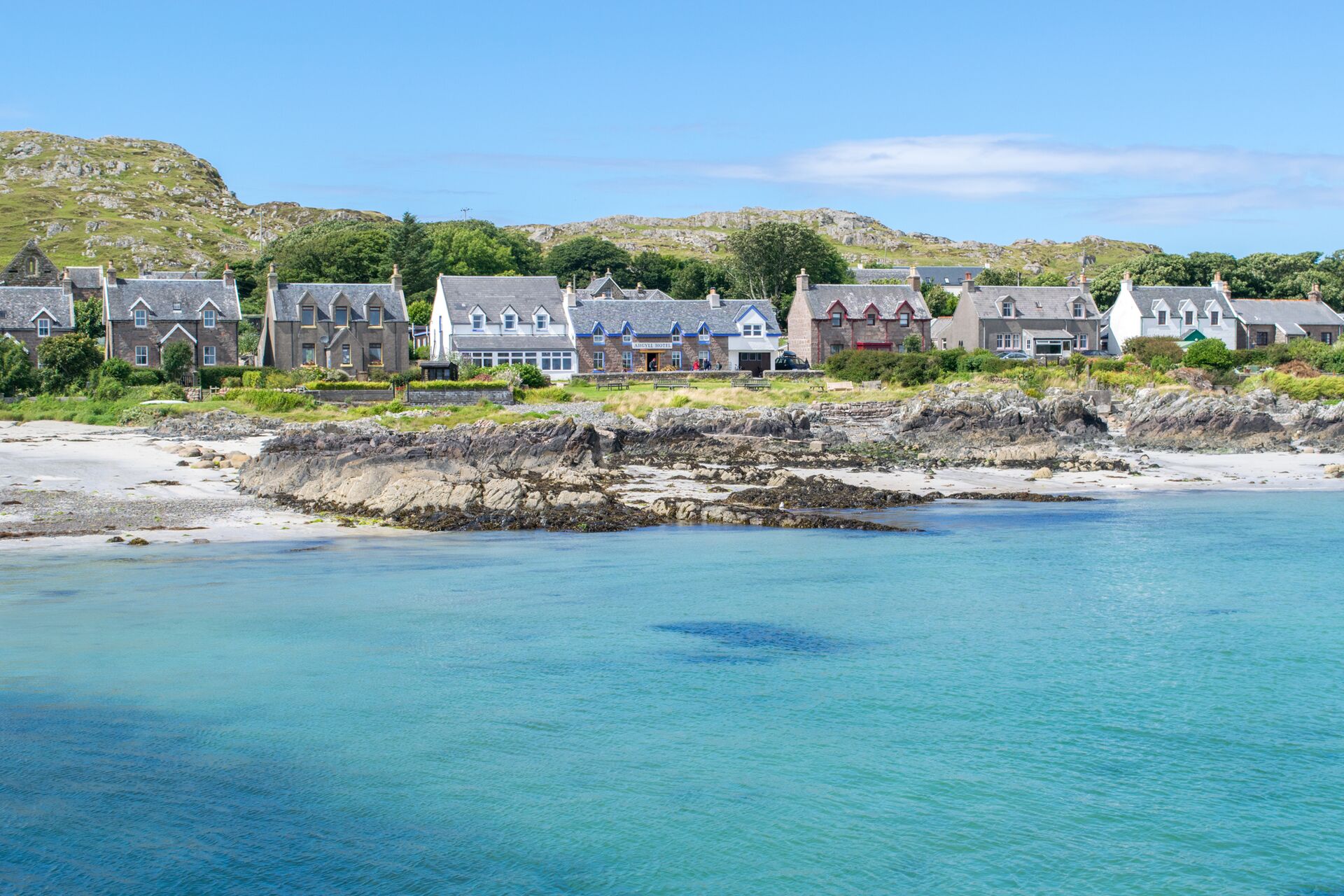 Isle of Iona with a sandy beach, turquoise waters gently lapping the shore, and traditional stone houses
