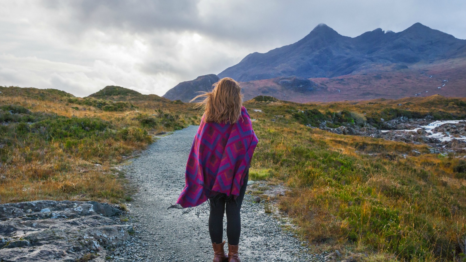 Young woman with a woolen shawl enjoying the dramatic, windswept scenery at Sligachan, with mountains in the background