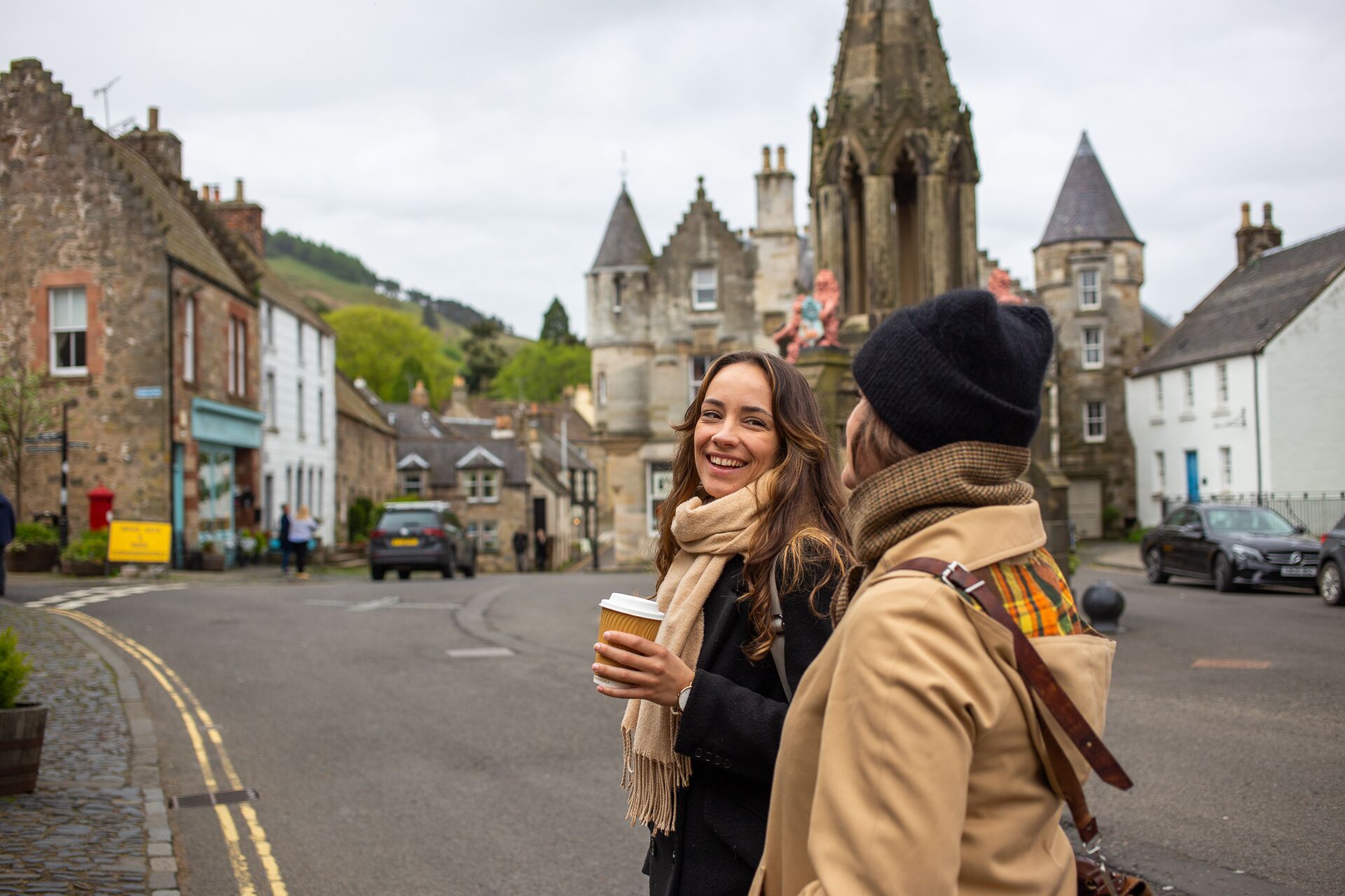 Two young women strolling through Falkland, passing historic stone buildings and charming streets