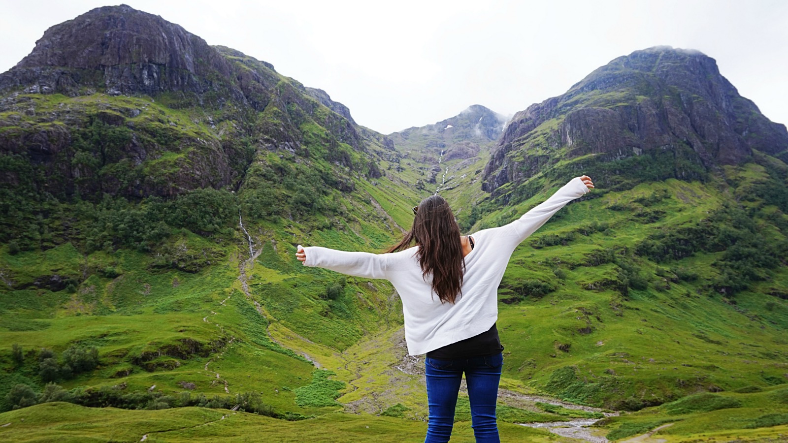 Young woman with arms outstretched taking in the dramatic mountains and valleys of Glen Coe