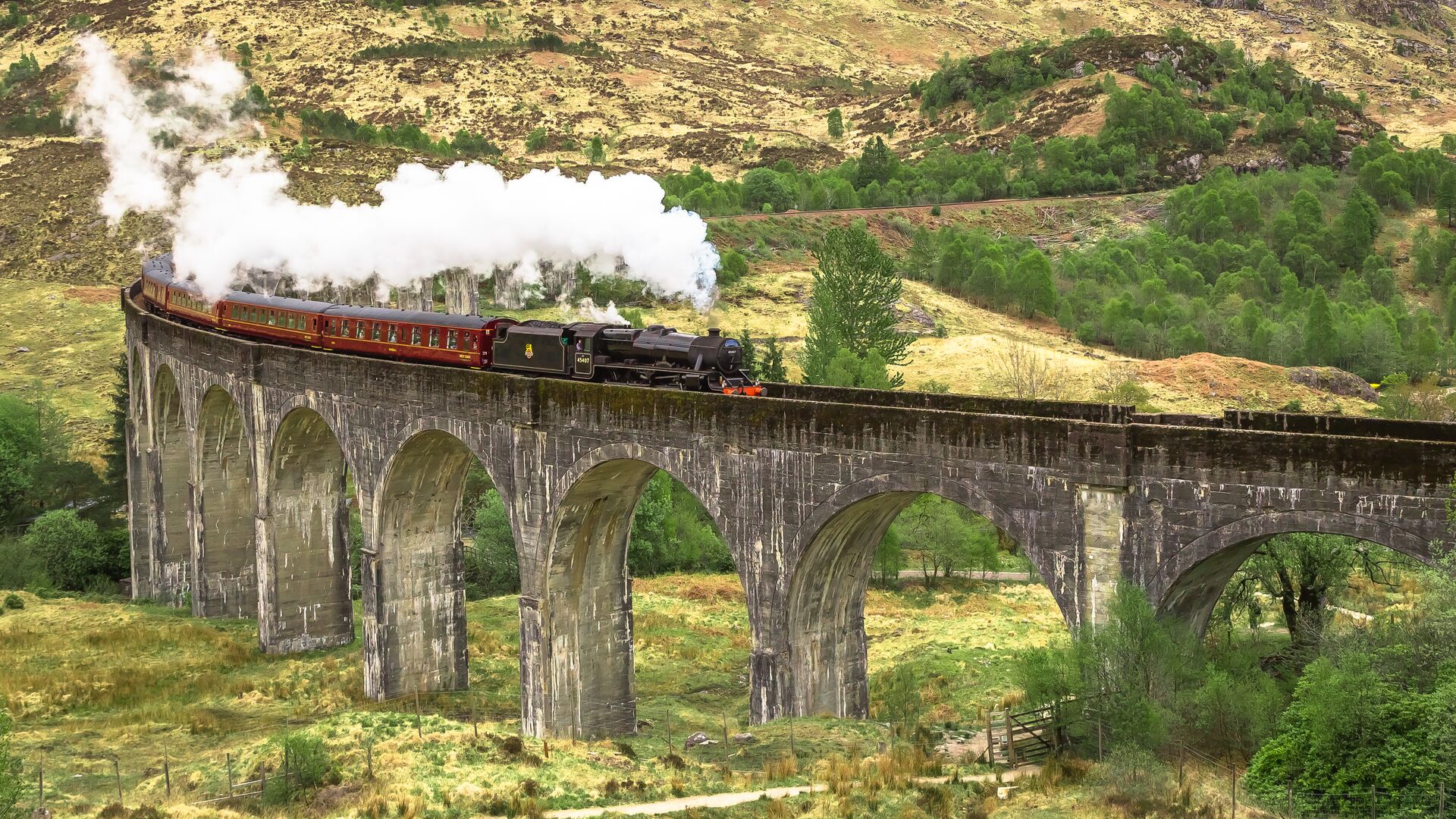 Jacobite SteaJacobite steam train crossing the Glenfinnan Viaduct with stunning Highland scenery in the backgroundm Train